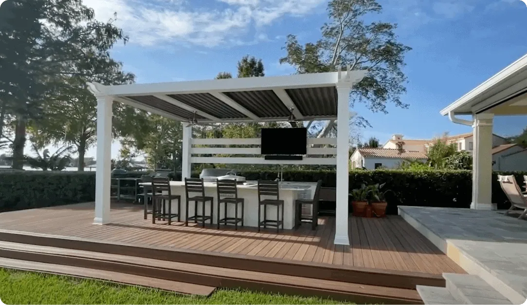 White motorized pergola over an outdoor bar and TV on a raised wood deck