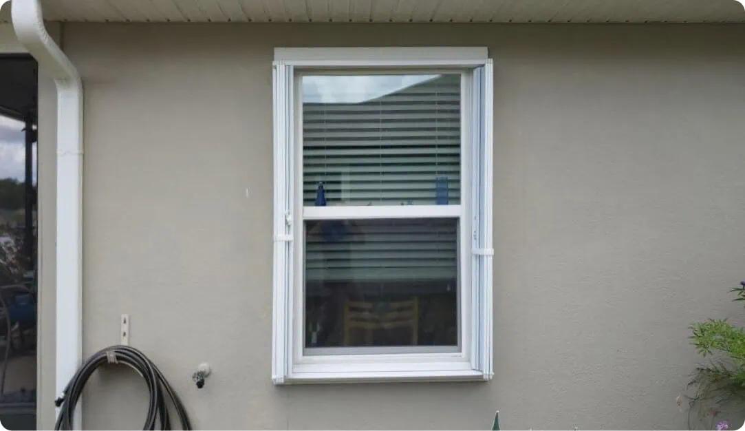 Double-hung window with white trim on a beige stucco home