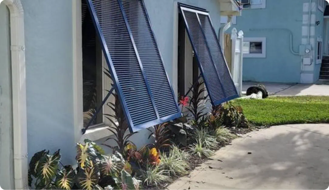 Navy Bahama shutters propped open on a light blue home beside a walkway