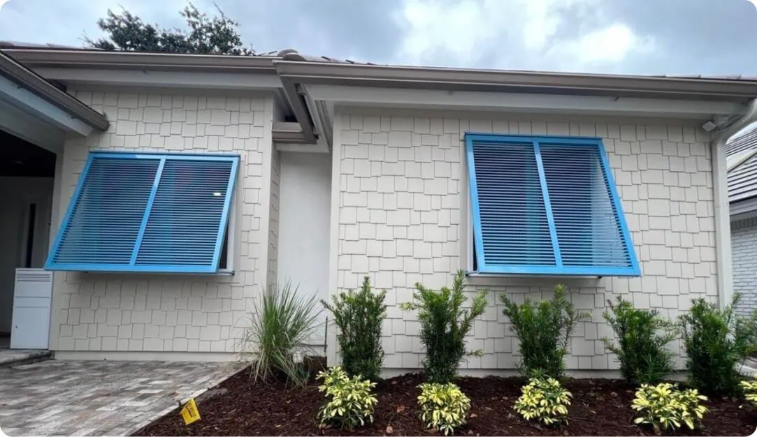 Light blue Bahama shutters on a white shingle-sided home