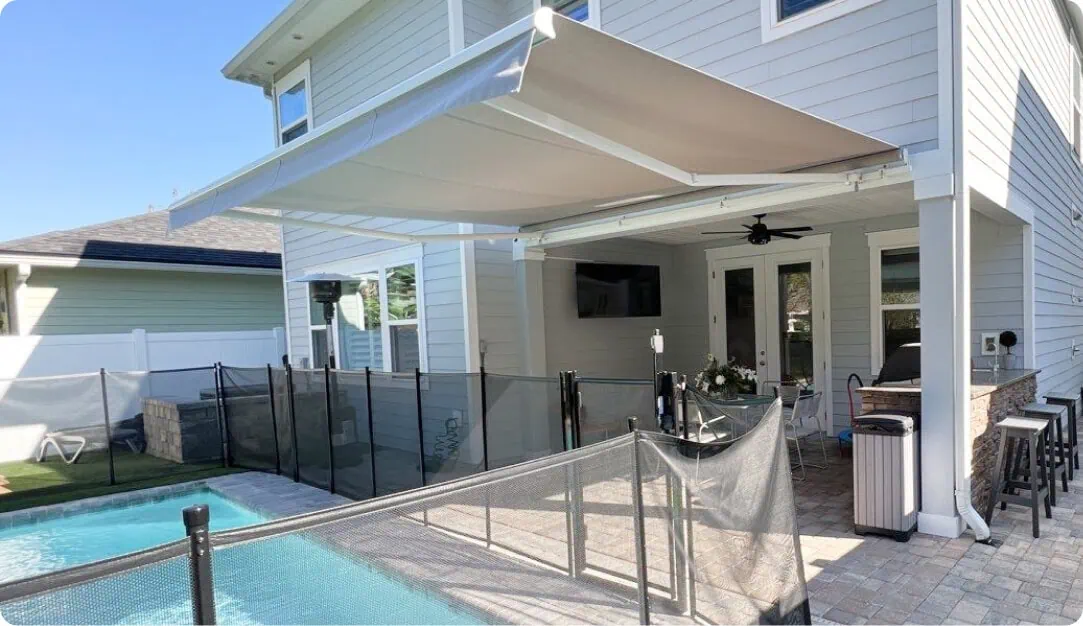 Retractable awning extended over a patio next to a fenced pool