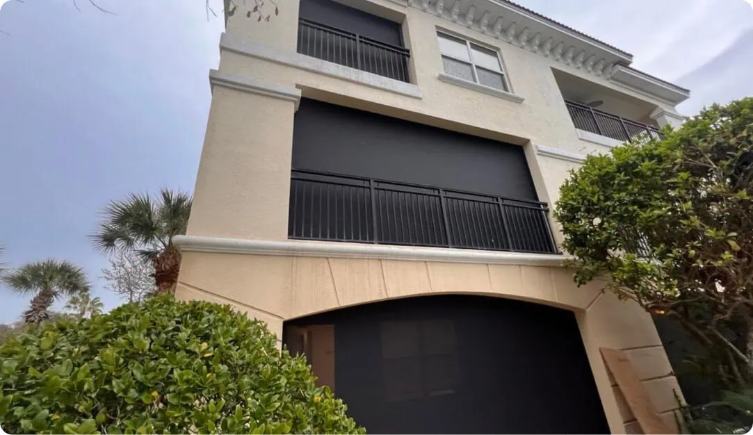 Dark retractable screens on the balconies of a cream stucco home